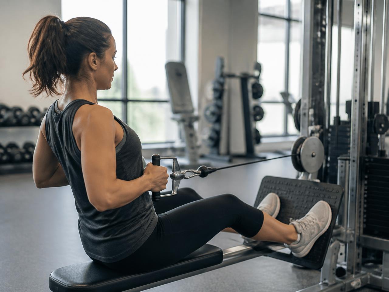 A woman performing a seated cable row in a daylit gym.